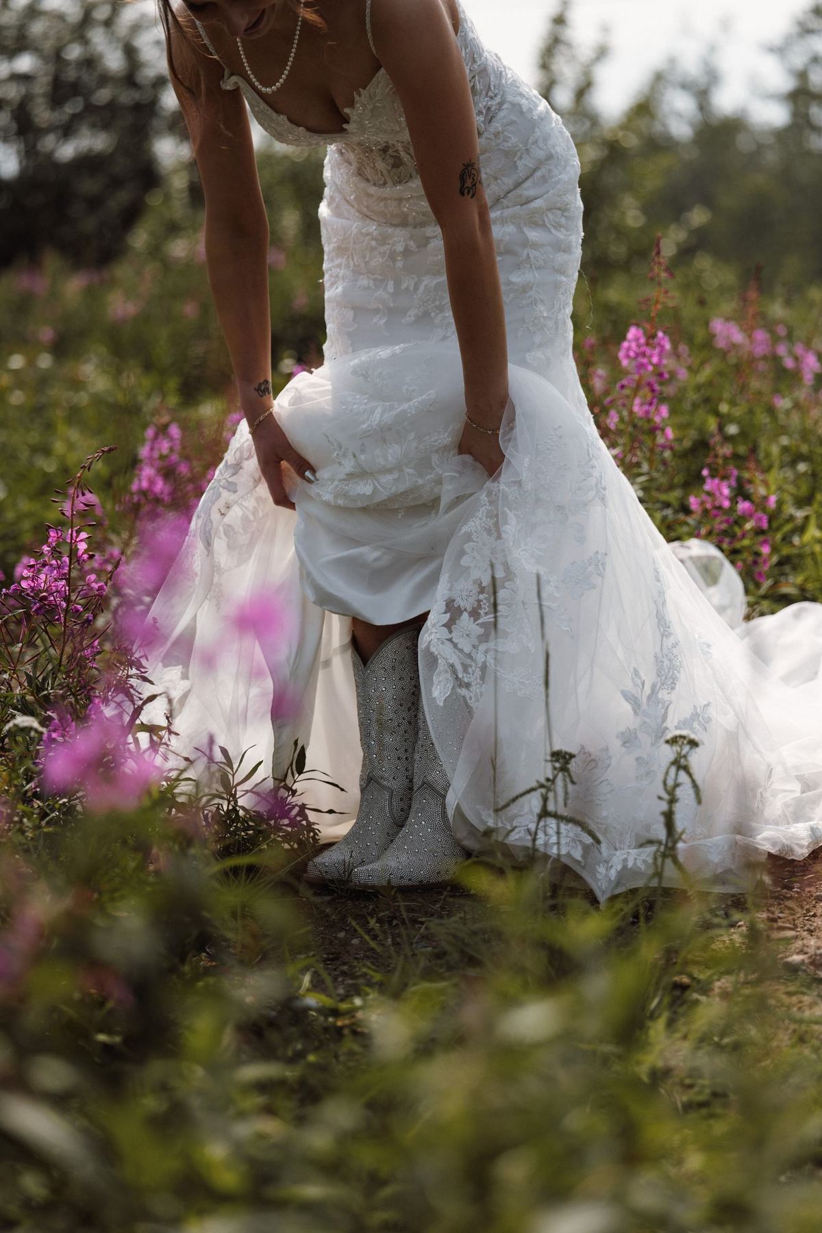 Bride from behind wading through a field of fireweed in her lace gown