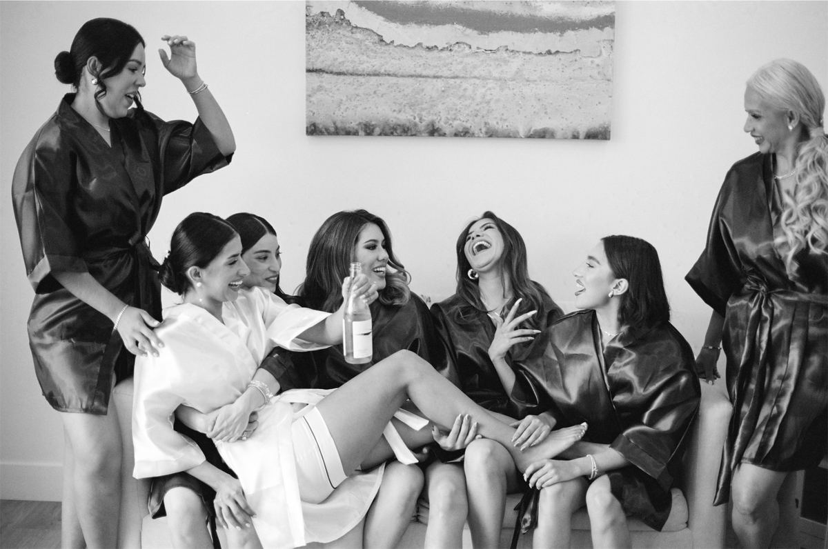 Black and white of the bride and her bridesmaids laughing in silk robes while getting ready