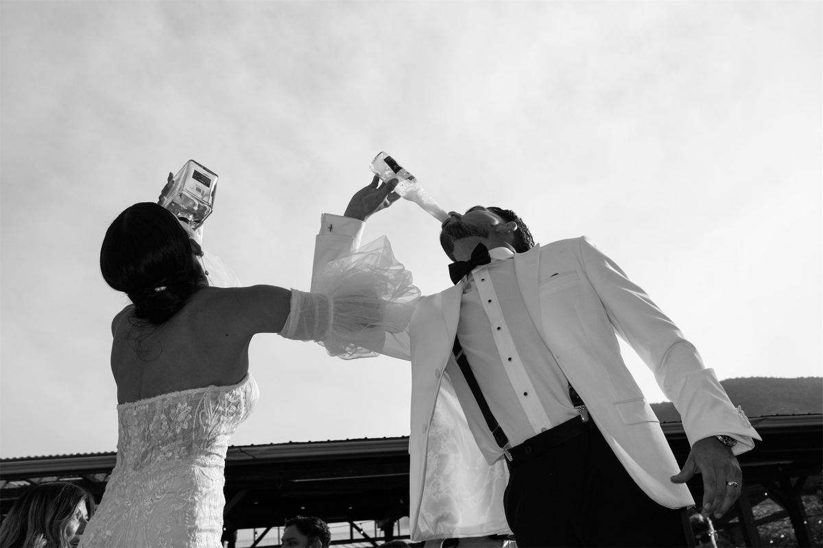 Black and white shot of the newlyweds drinking champagne straight from the bottles