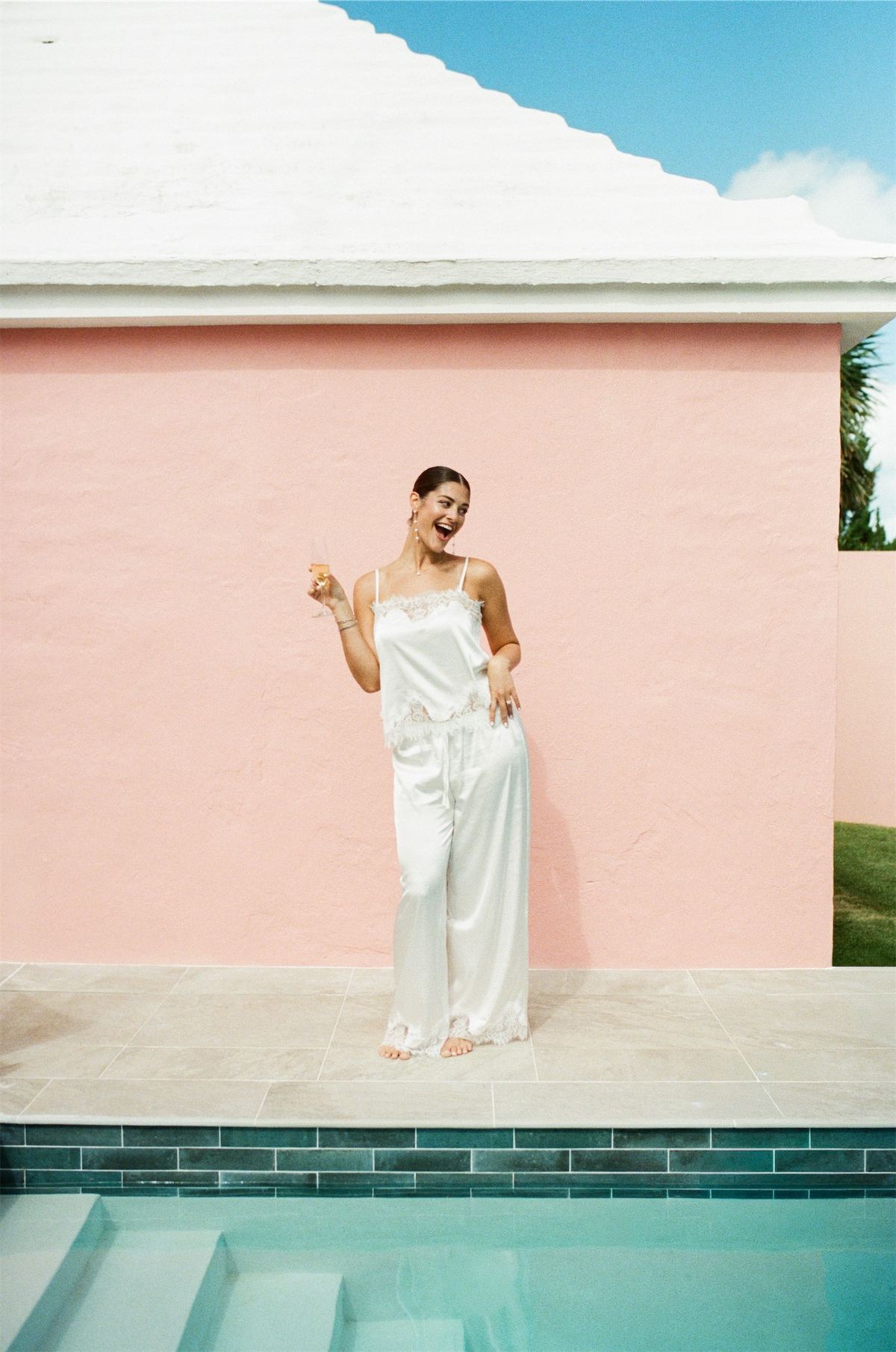 Bride in a satin slip dress dancing beside the pool against a coral pink wall