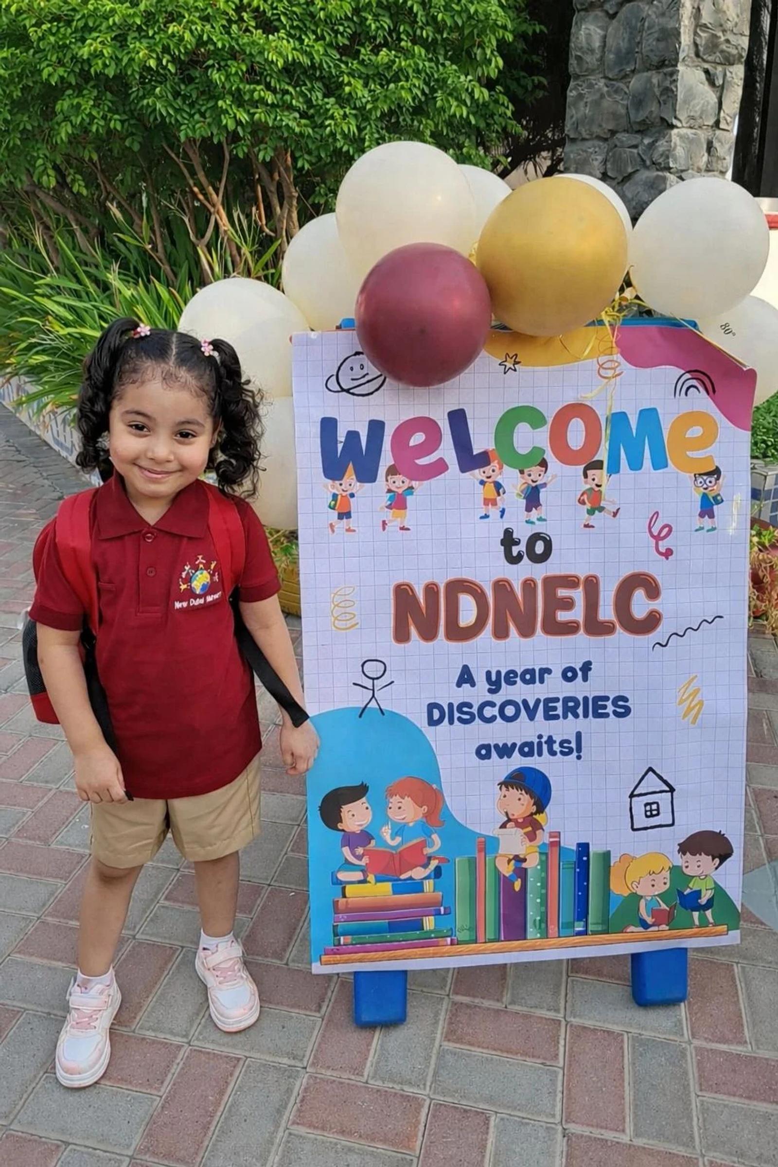 A smiling child beside the nursery welcome sign