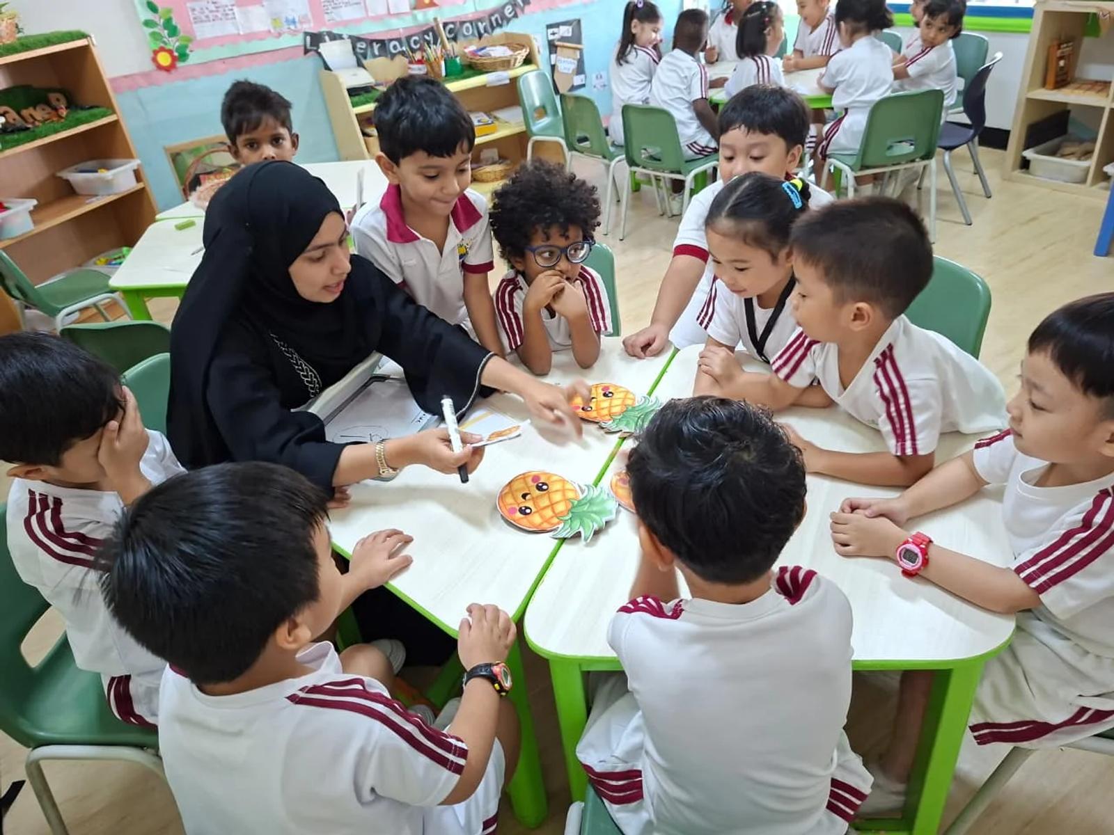 A teacher guiding children through a table activity in the nursery classroom