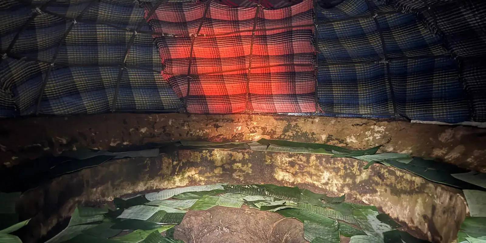 Interior of a Temazcal sweat lodge with glowing volcanic stones and ceremonial herbs, opening onto Mexican mountains at golden hour