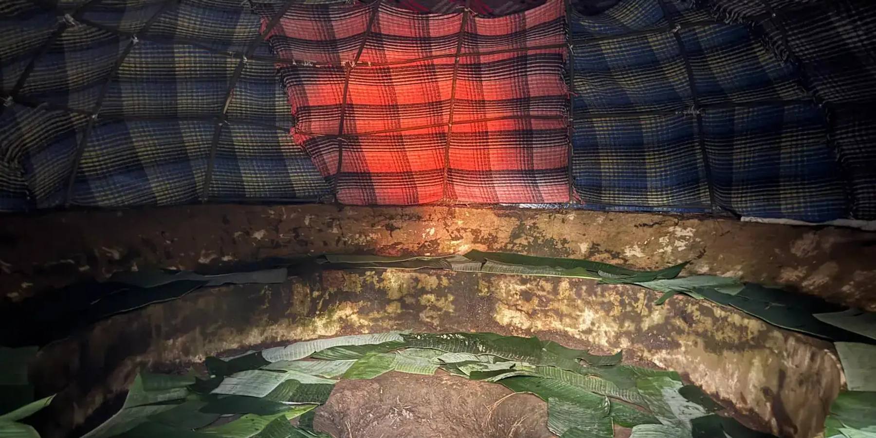 Interior of a Temazcal sweat lodge with glowing volcanic stones and ceremonial herbs, opening onto Mexican mountains at golden hour