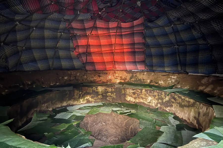 Interior of a Temazcal sweat lodge with glowing volcanic stones and ceremonial herbs, opening onto Mexican mountains at golden hour