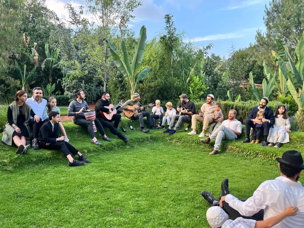 An outdoor kumsits — the Attesi community gathered on the lawn with guitars near Sabata