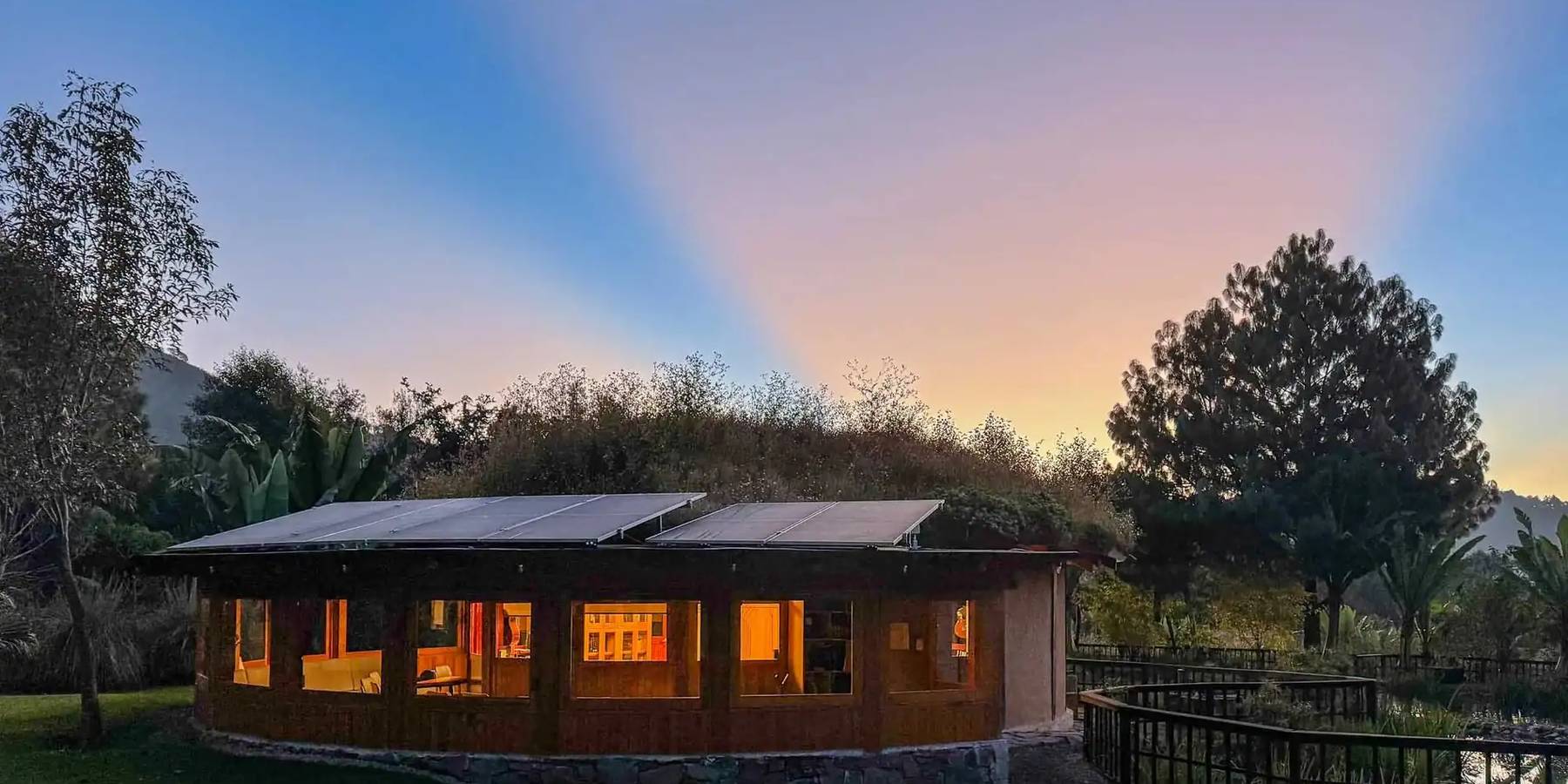 The Attesi eco-building glowing at dusk beside the reflecting pond, framed by mountains