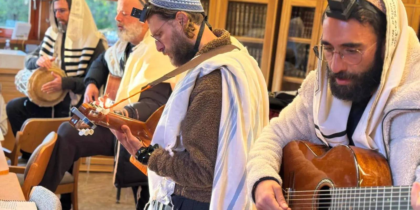 Members of the Attesi community praying with tallit and tefillin, accompanied by guitar and hand drum, in the midrash study hall