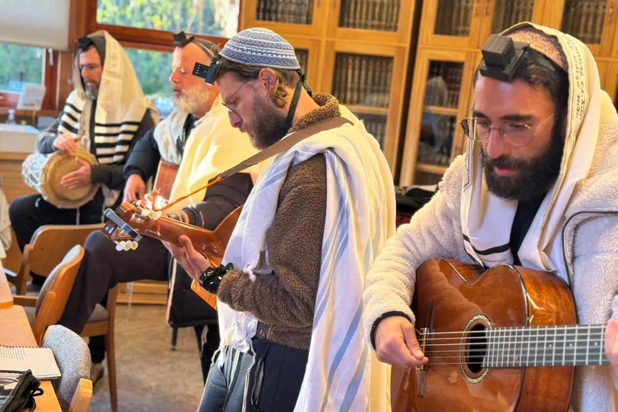 Members of the Attesi community praying with tallit and tefillin, accompanied by guitar and hand drum, in the midrash study hall
