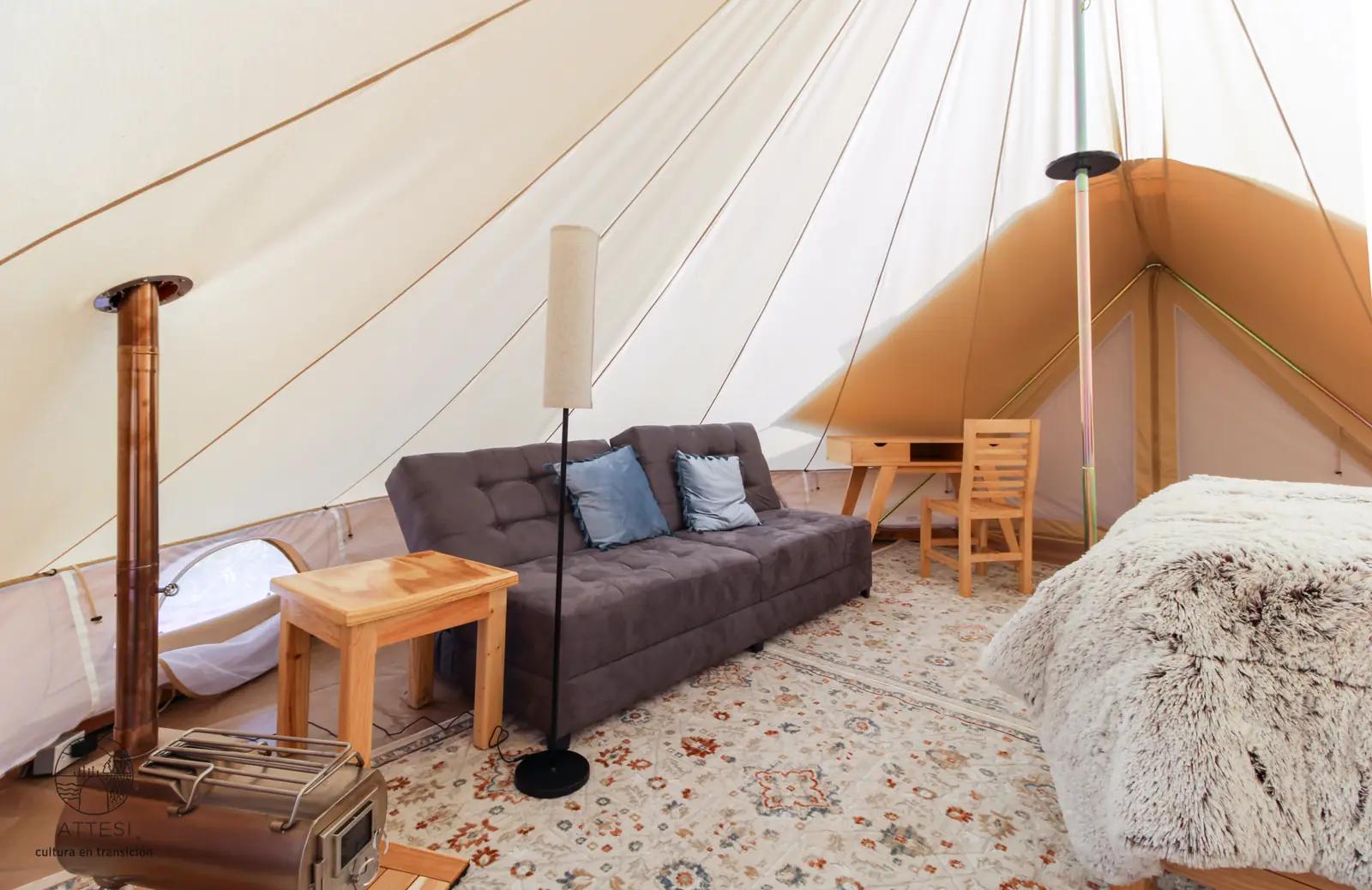 Interior of an Attesi glamping tent with a sofa, wood stove, and bed