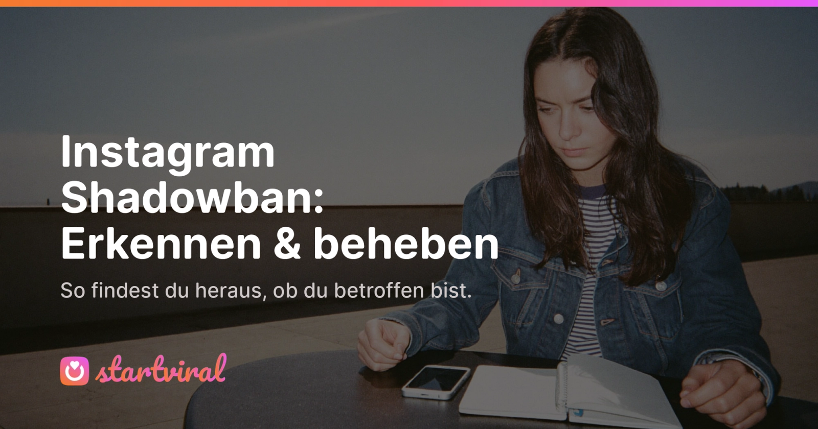 Frau sitzt auf einer Dachterrasse an einem Tisch und blickt nachdenklich auf ihr Smartphone.