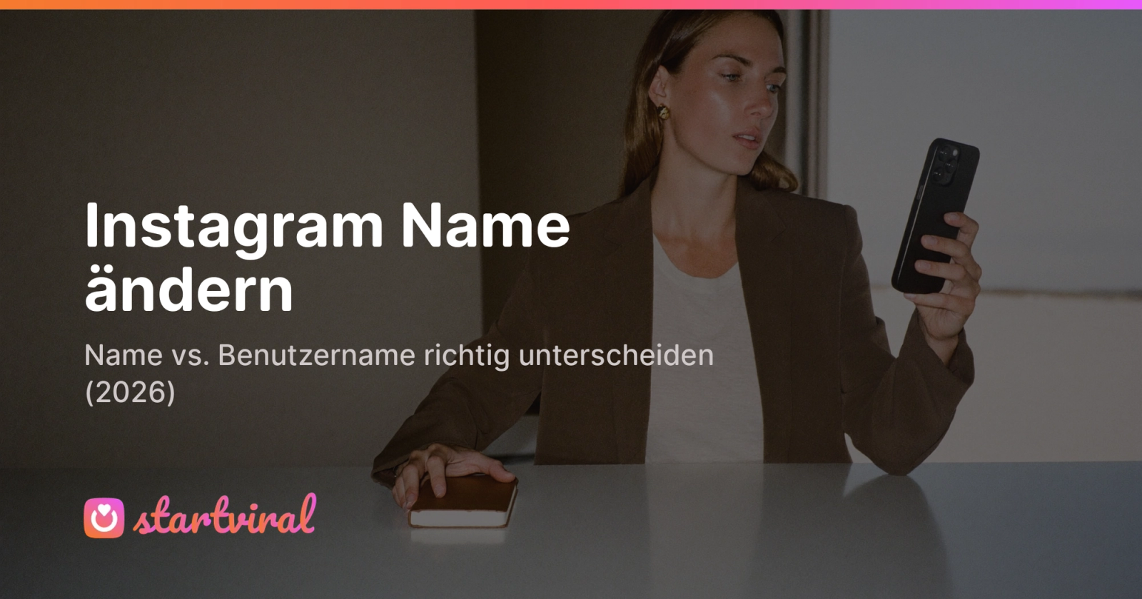 Frau sitzt an einem Tisch vor einer Studio-Kulisse und schaut auf ihr Smartphone mit dunklem Bildschirm.
