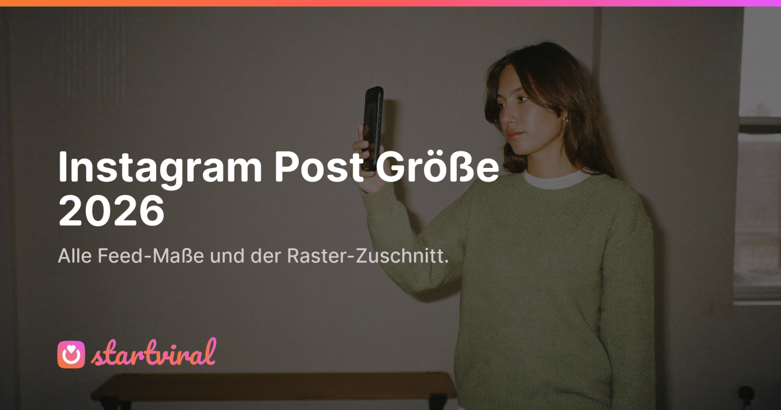 Frau im grünen Strickpullover prüft in einem hellen Studio ein Foto auf ihrem Smartphone.