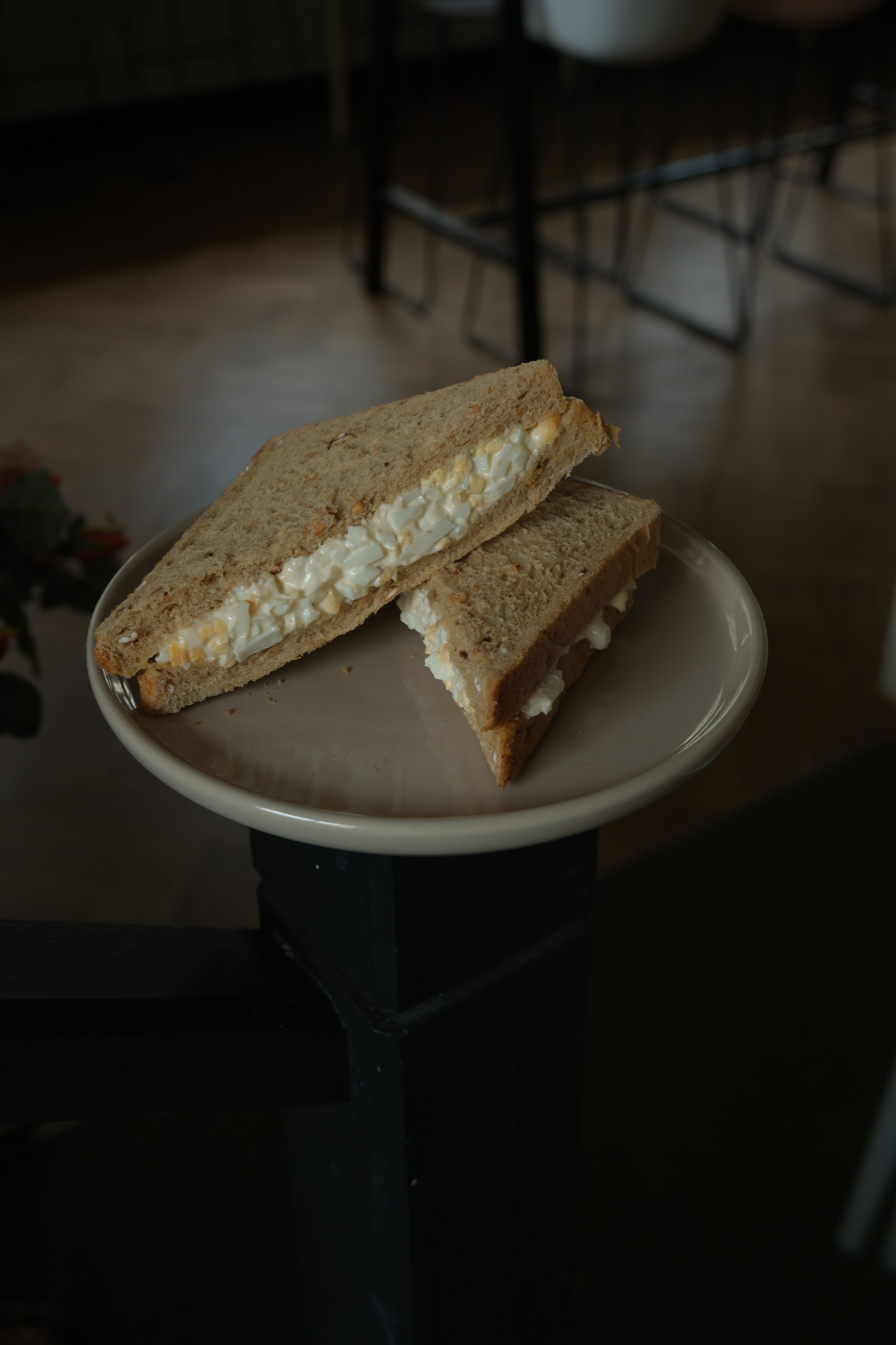 Two halves of an egg salad sandwich on whole-grain bread, on a beige plate.