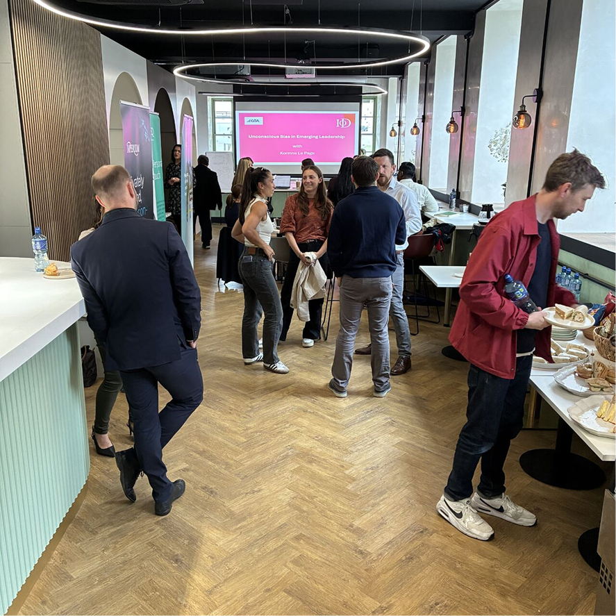 Attendees mingle and enjoy refreshments at a workshop on "Unconscious Bias in Emerging Leadership" in a modern venue.