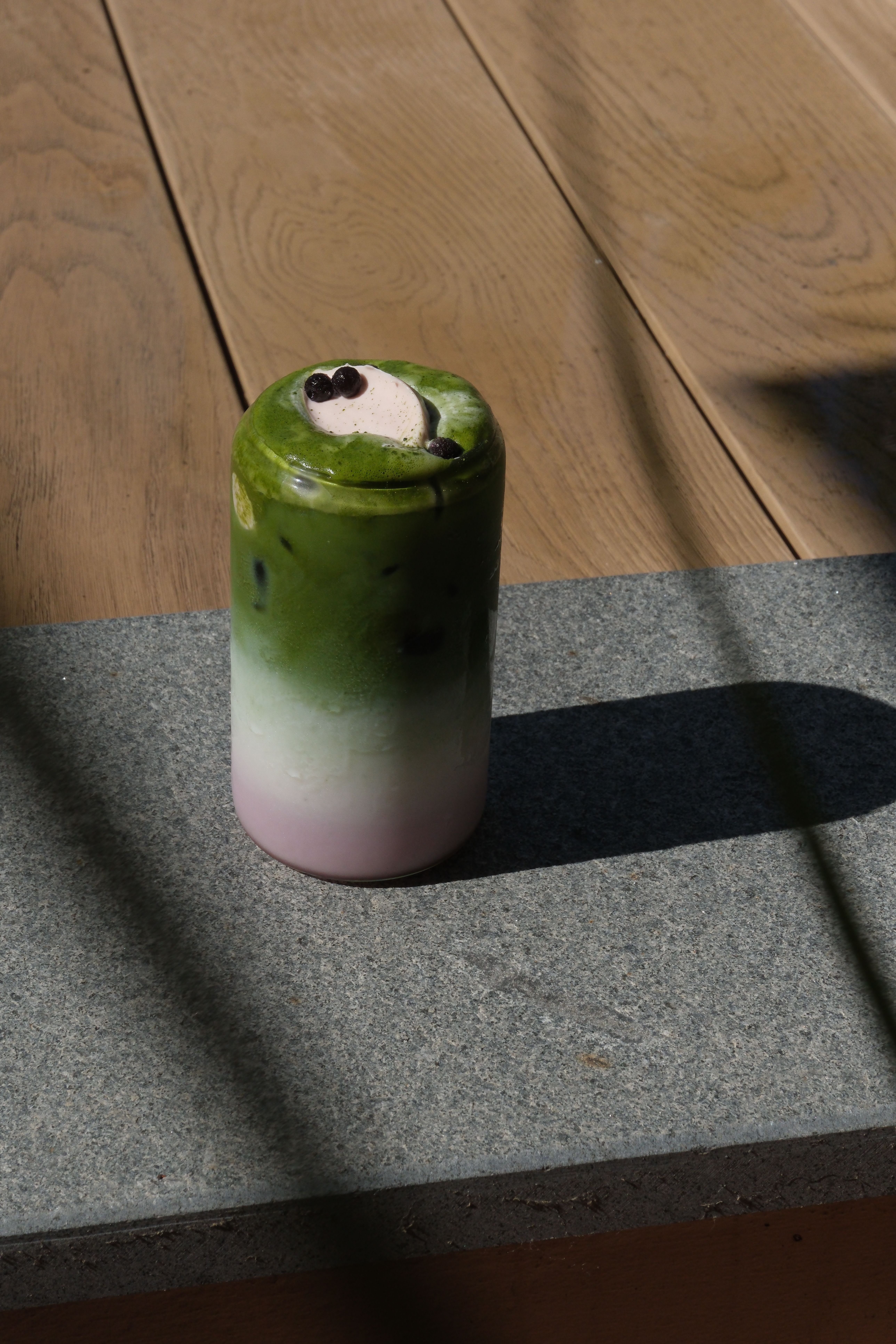 A tall glass of layered pink, white, and matcha green drink, topped with cream and sprinkles.