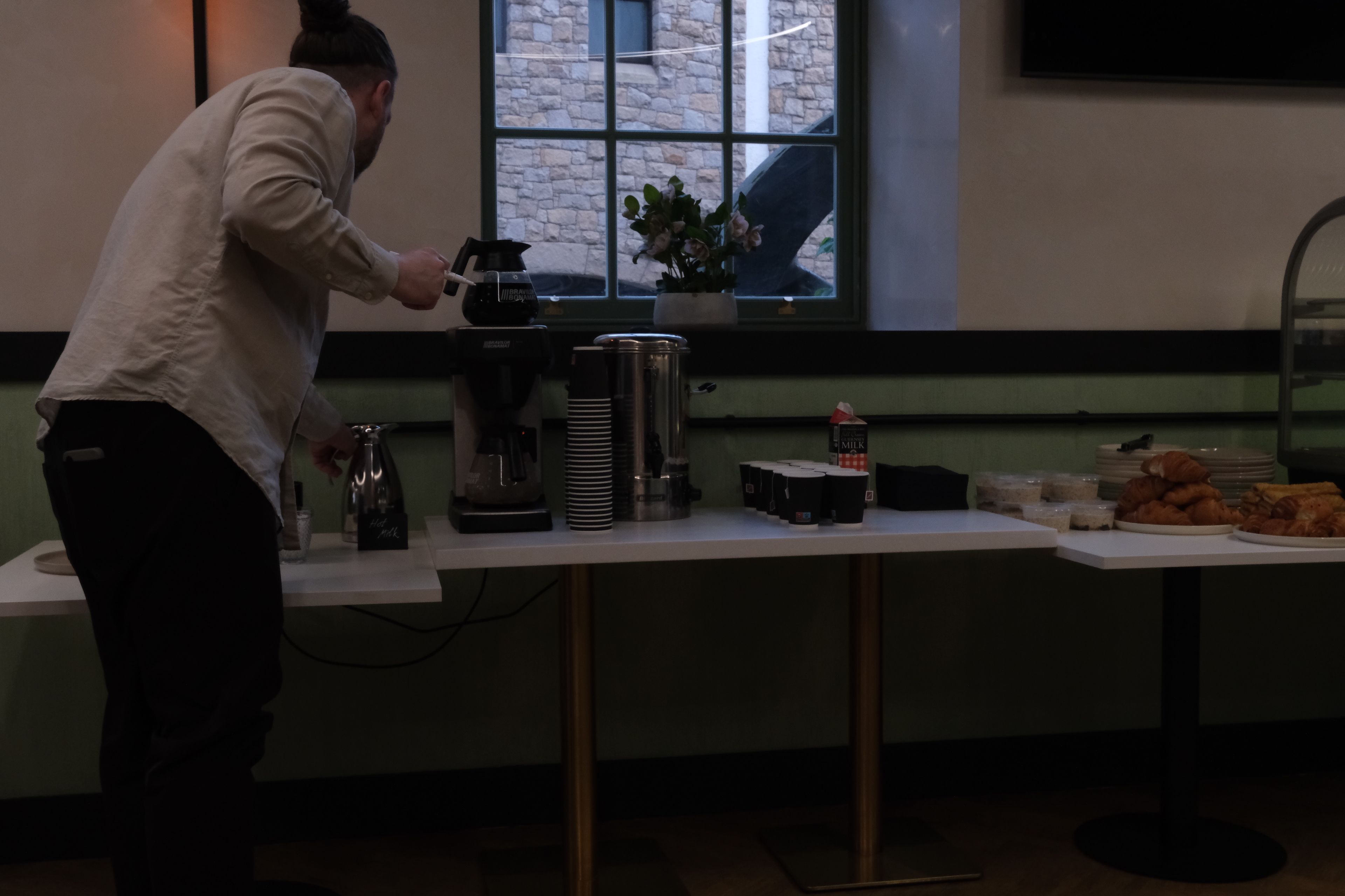 A man prepares coffee at a beverage station with pastries.