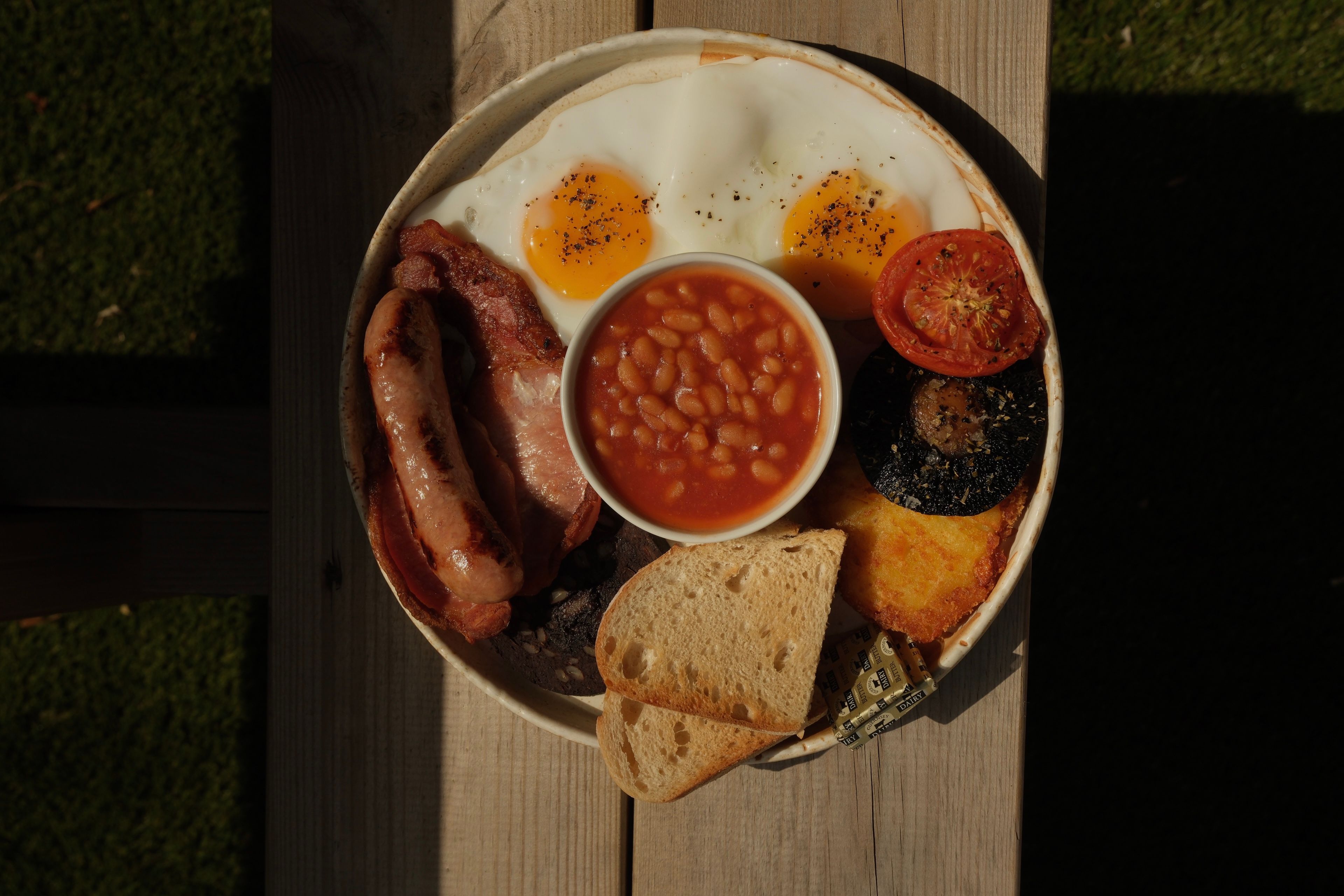 A full cooked breakfast on a plate with bacon, sausages, eggs and toast