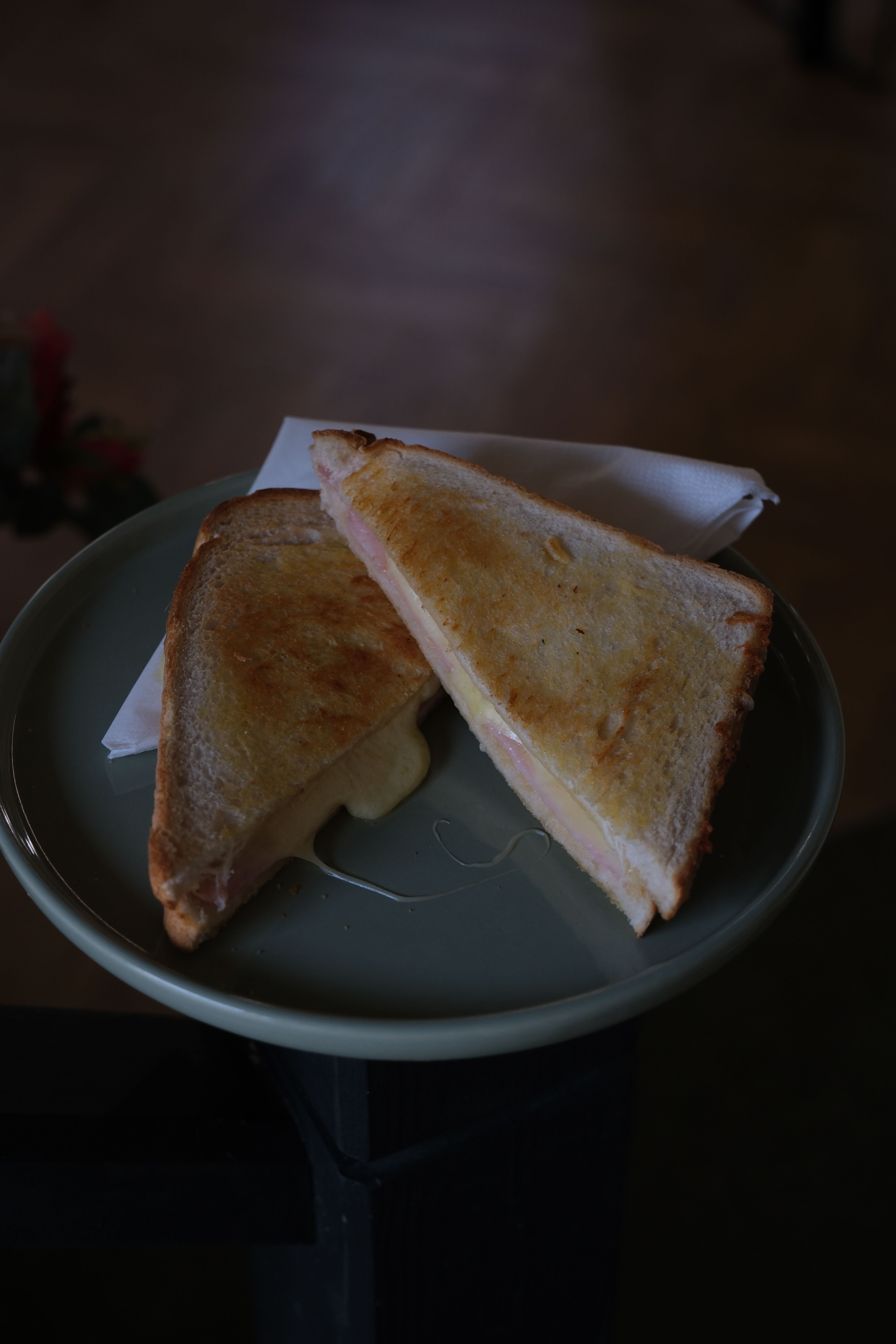 Two grilled cheese and ham sandwiches on a plate, one with melted cheese oozing out.