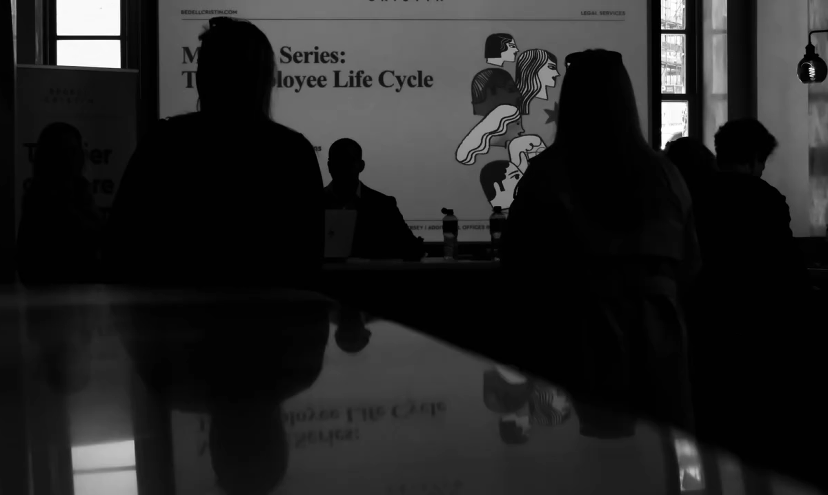 Silhouetted people in a dimly lit room facing a screen displaying "The Employee Life Cycle."