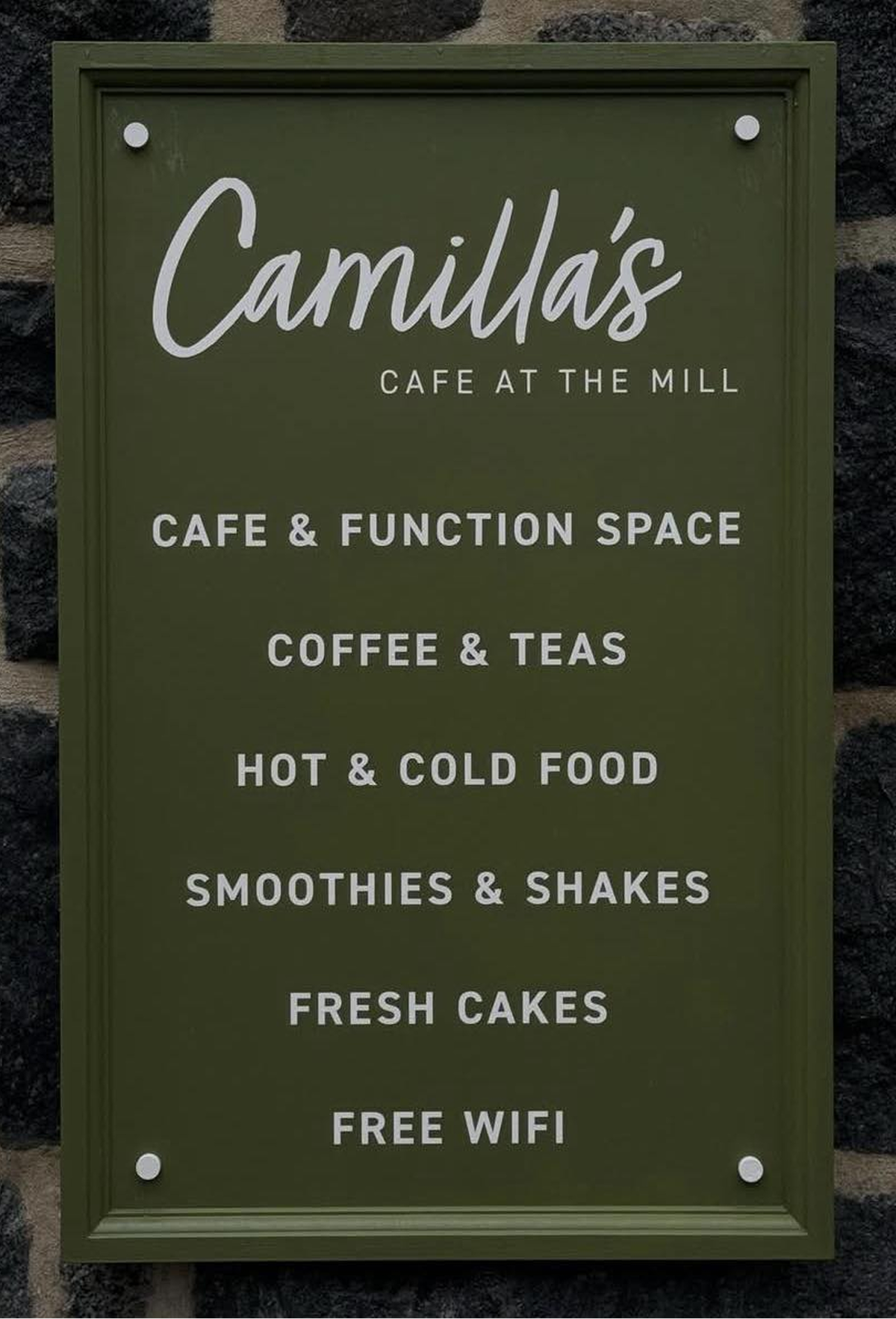 A dark green sign for Camilla's Cafe at the Mill, listing: Cafe & Function Space, Coffee & Teas, Hot & Cold Food, Smoothies & Shakes, Fresh Cakes, Free Wifi.