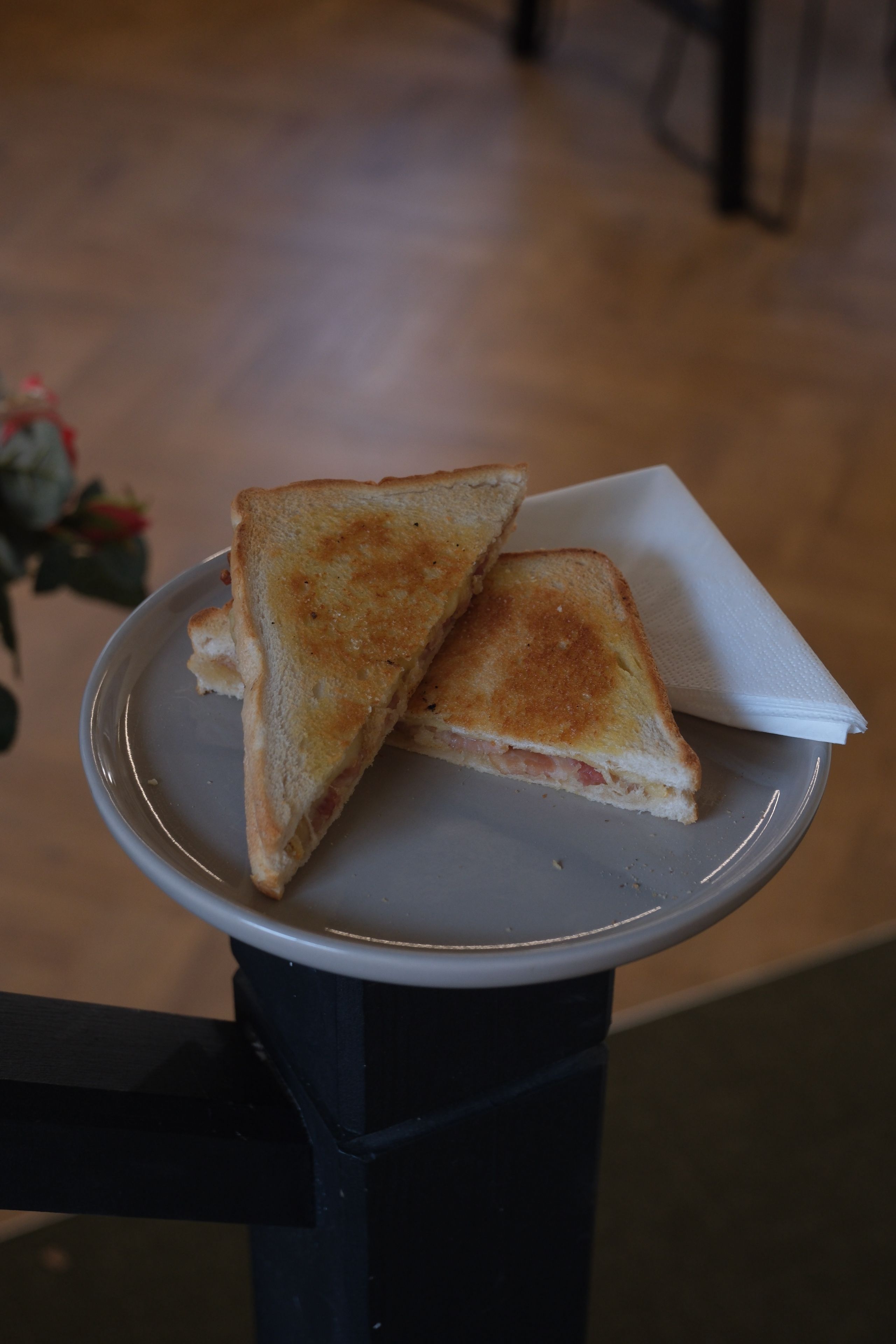 Two grilled ham and cheese sandwich halves and a white napkin on a grey plate.