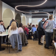 A group of people attending a "Townhall" event in a modern room with arched doorways and a wavy ceiling light.