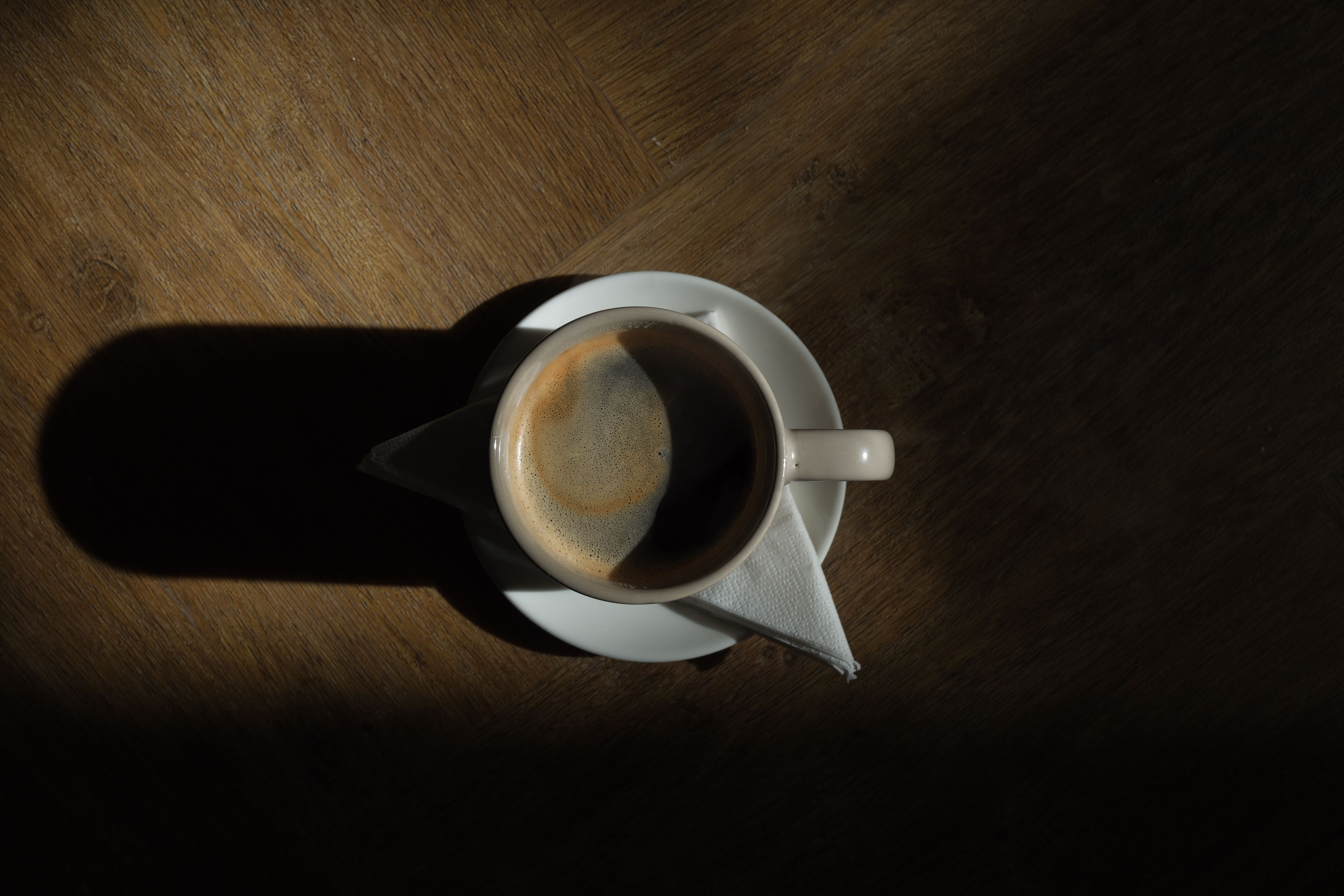 Coffee cup with crema and a long shadow on a wooden table.