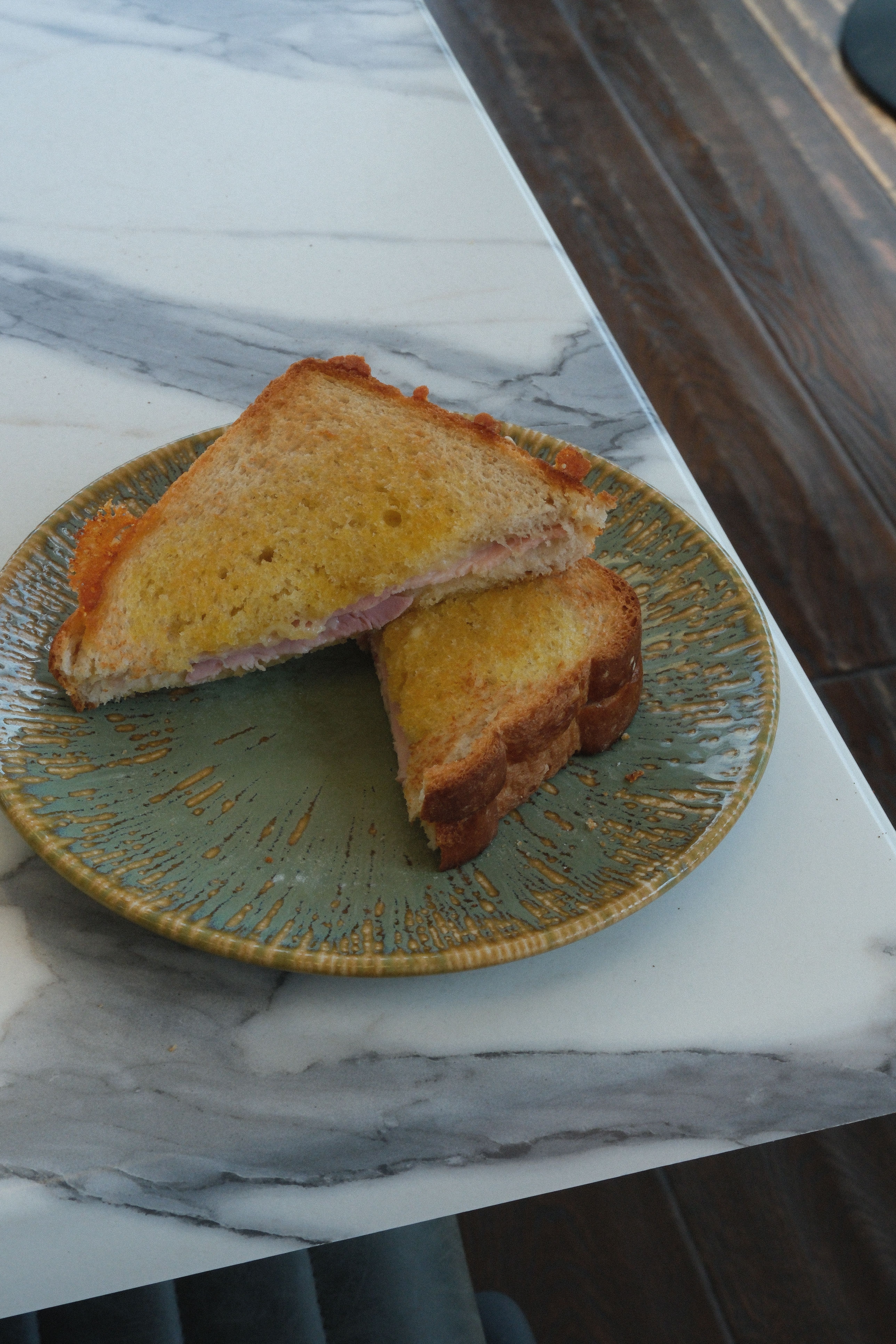 A ham and cheese toastie, cut in half, on a green plate.
