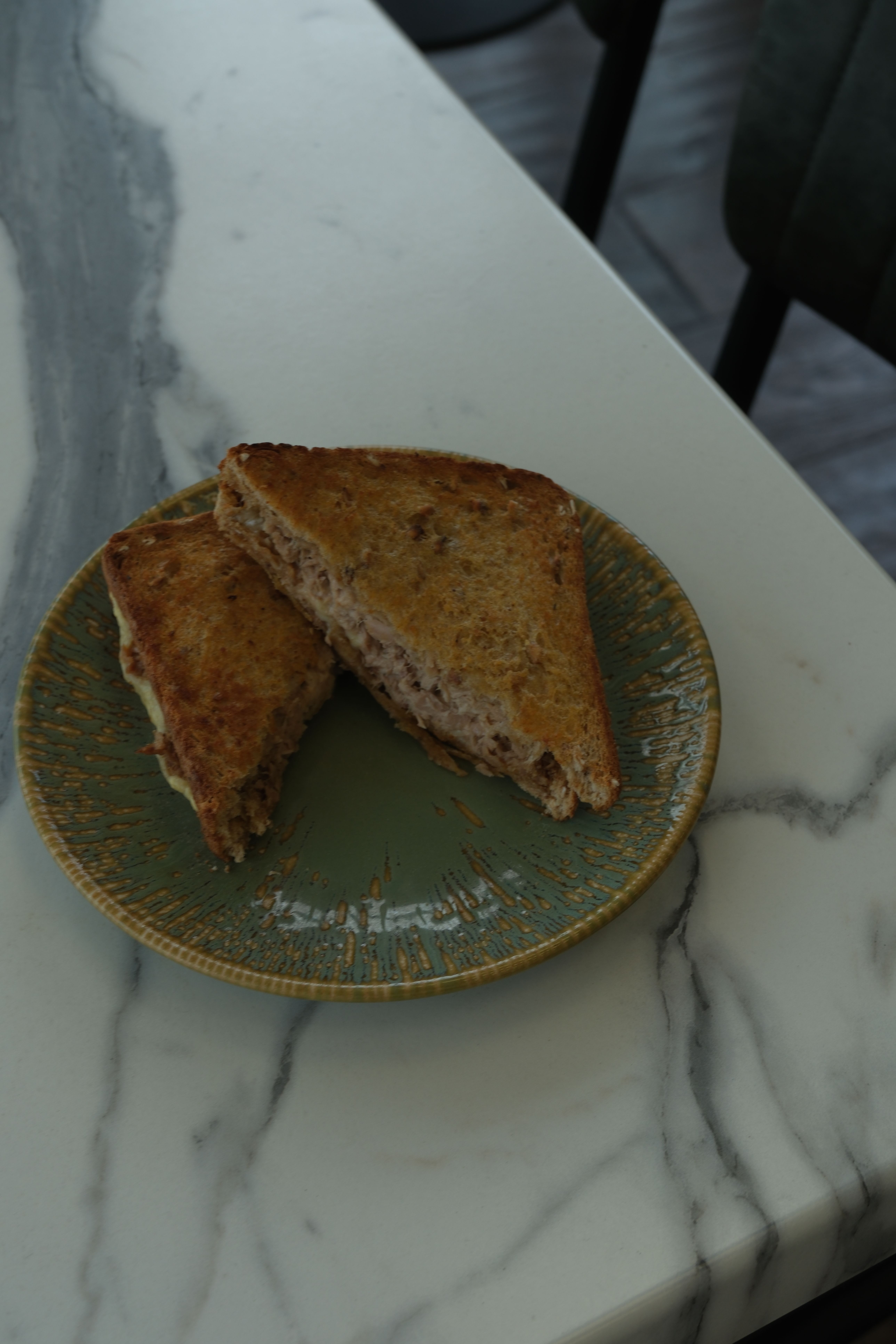 Toasted tuna sandwich cut in half on a green plate on a marble table.