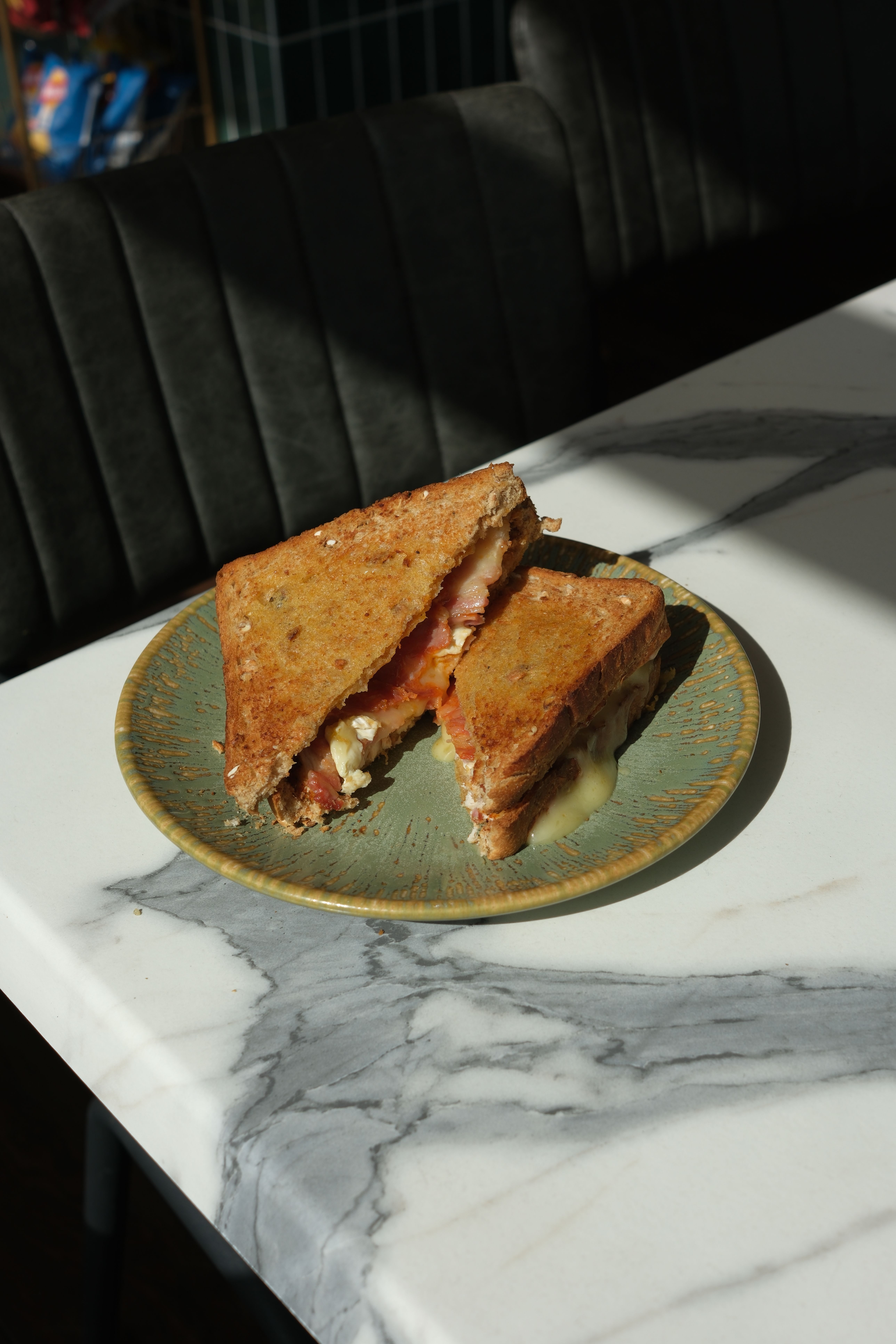 A grilled bacon and cheese sandwich, cut into two halves, on a green plate.