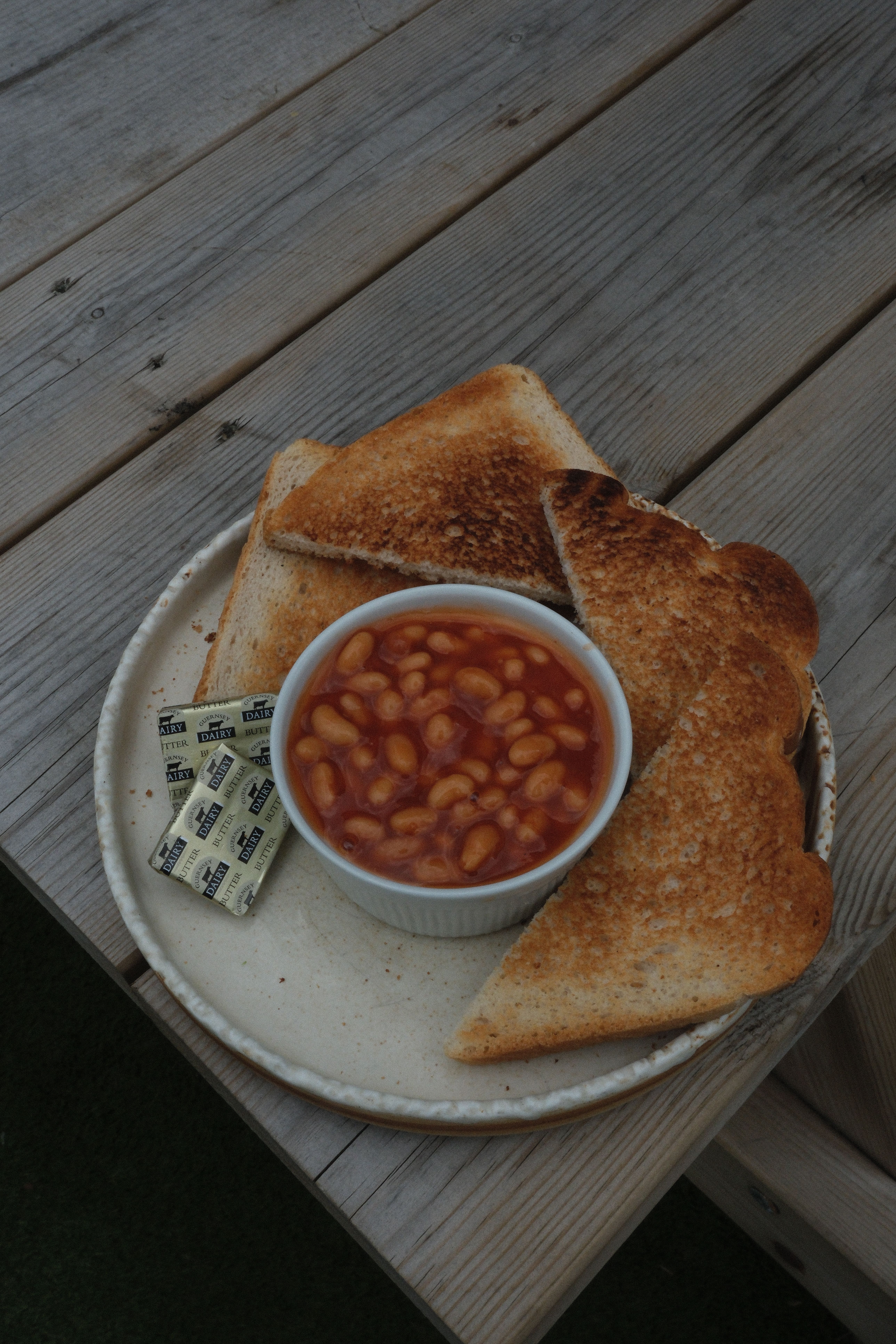 A plate with baked beans, toast, and butter on a wooden table.
