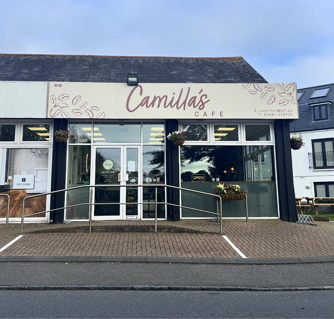 Exterior view of Camilla's Cafe with a light-colored sign, large windows, and a glass entrance, bordered by a sidewalk.
