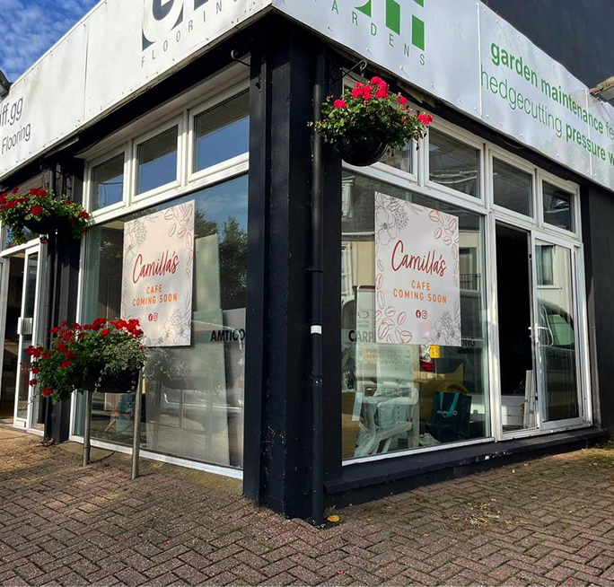 Shopfront with "Camilla's Cafe Coming Soon" signs in the windows, adorned with red flowers.