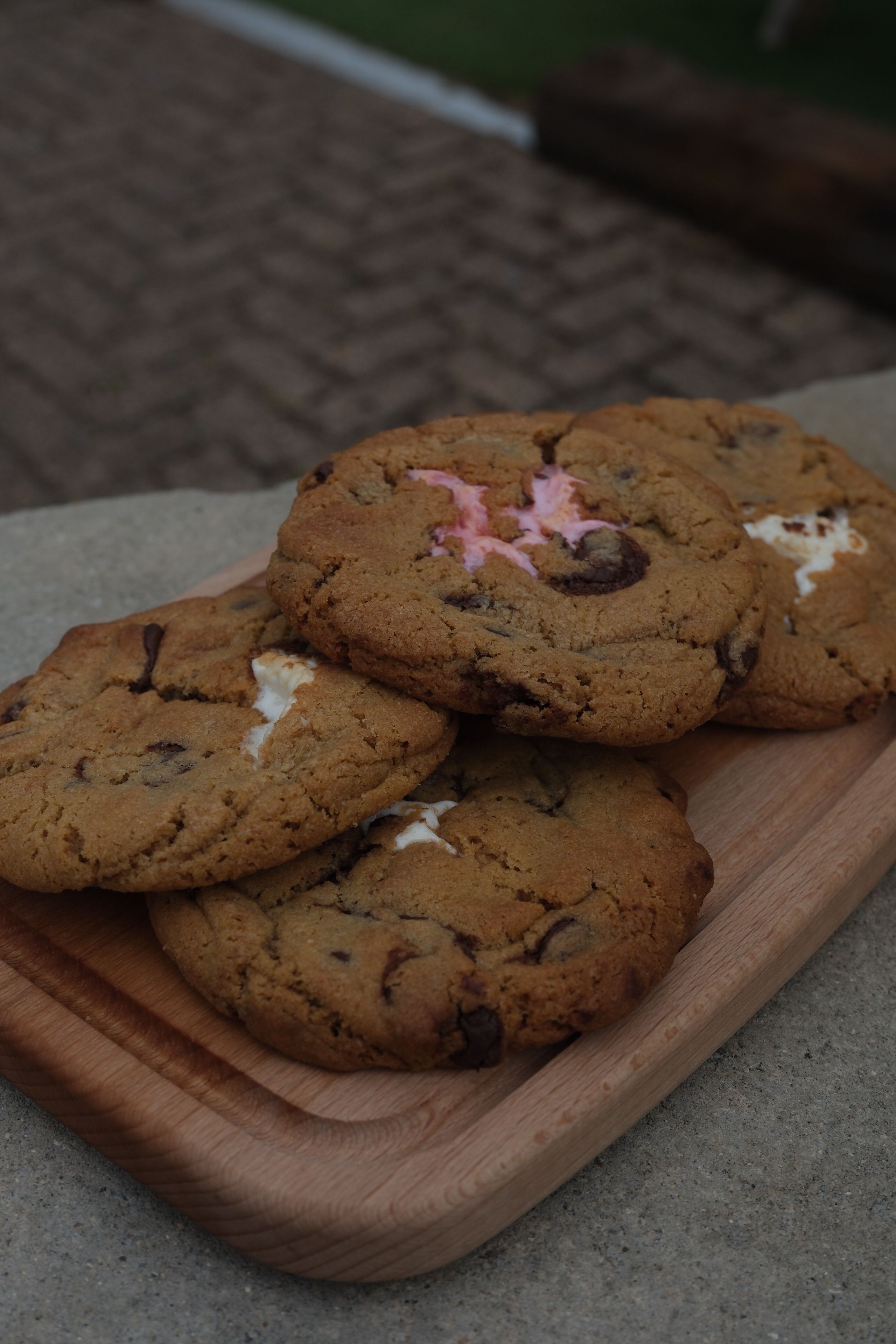 Chocolate chip cookies with melted white and pink marshmallows on a wooden tray.