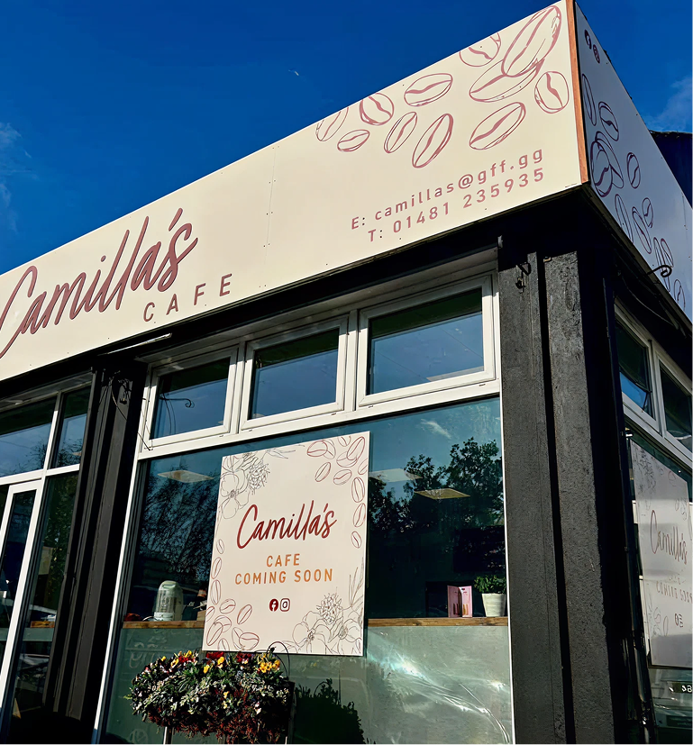 Exterior of Camilla's Cafe with a large sign, a "Coming Soon" banner in the window, and a floral hanging basket.