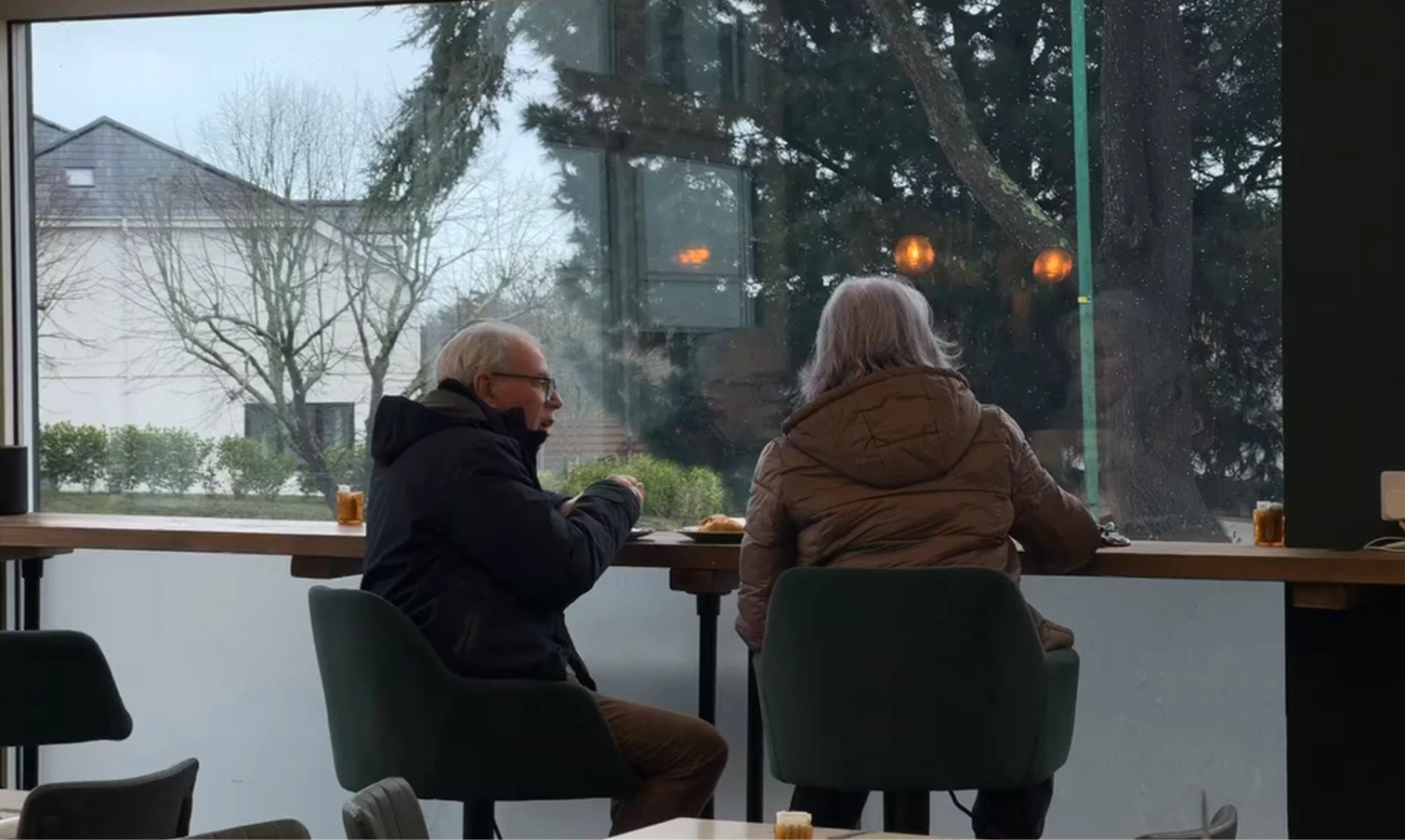 Two older people eating at a window bar looking out at an overcast day.