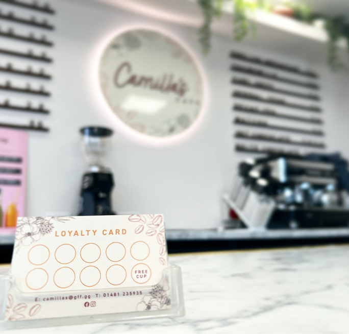 White loyalty card with 10 empty stamp circles and "FREE CUP" text, displayed at Camilla's Cafe.