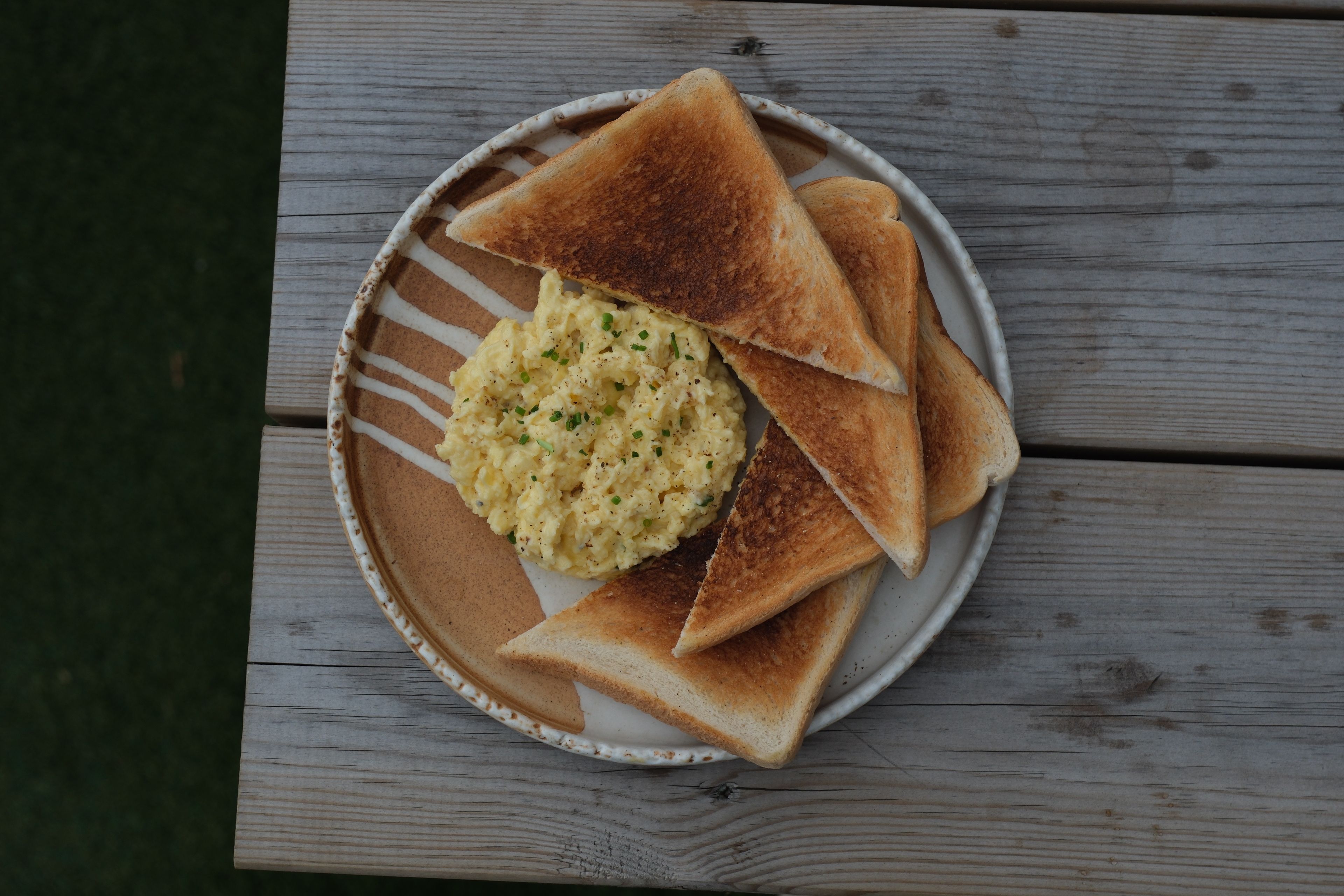 Scrambled eggs with chives and toast triangles on a plate, on a wooden table.
