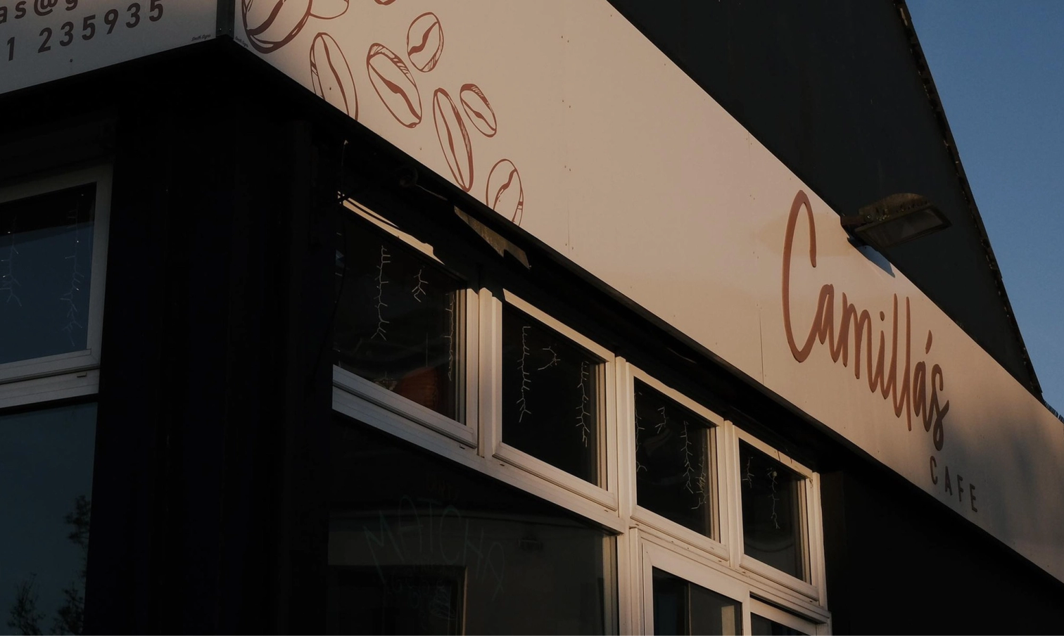 Exterior view of Camilla's CAFE sign with coffee bean illustrations on a dark building.