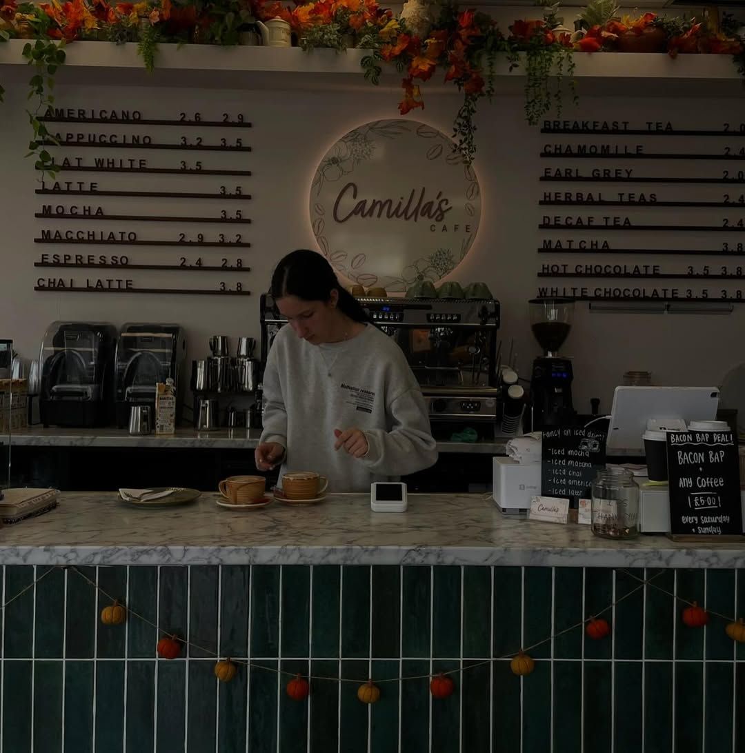 A barista prepares drinks at Camilla's Cafe, which is decorated with autumn foliage and a pumpkin garland.
