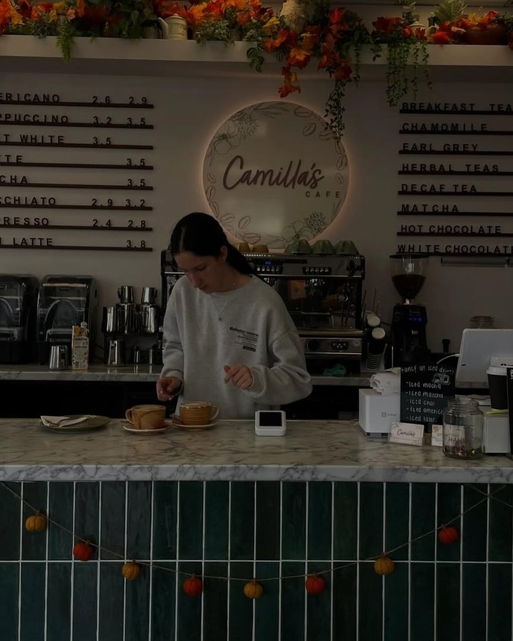 A barista prepares drinks at Camilla's Cafe, which is decorated with autumn foliage and a pumpkin garland.