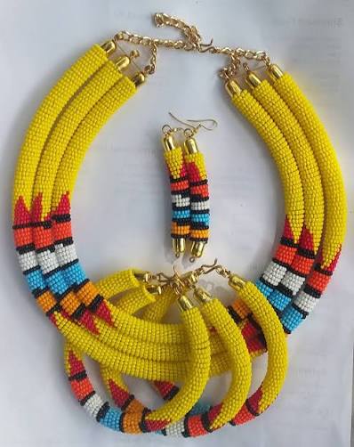 Bright, bold, and full of culture, this handcrafted African beaded jewelry set is designed to make a statement. Made with high-quality seed beads in vibrant yellow, red, black, blue, white, and orange, the necklace and matching earrings reflect traditional African artistry with a modern twist. The layered necklace sits beautifully on the neckline, while the matching drop earrings complete the look with elegance. Perfect for weddings, cultural events, parties, or as a standout accessory to elevate everyday fashion. Material: Glass seed beads, metal clasp Colors: Yellow base with multicolor patterns (red, black, blue, white, orange) Includes: 1 statement necklace + 1 pair of earrings Handmade in Africa This set is not just jewelry, it’s wearable art that celebrates African heritage.