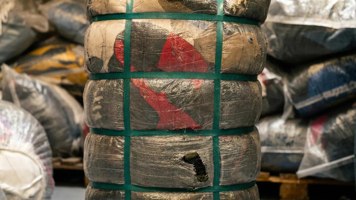 Close-up van een geperste tweedehands kleding baal met spanbanden, met meer balen erachter gestapeld