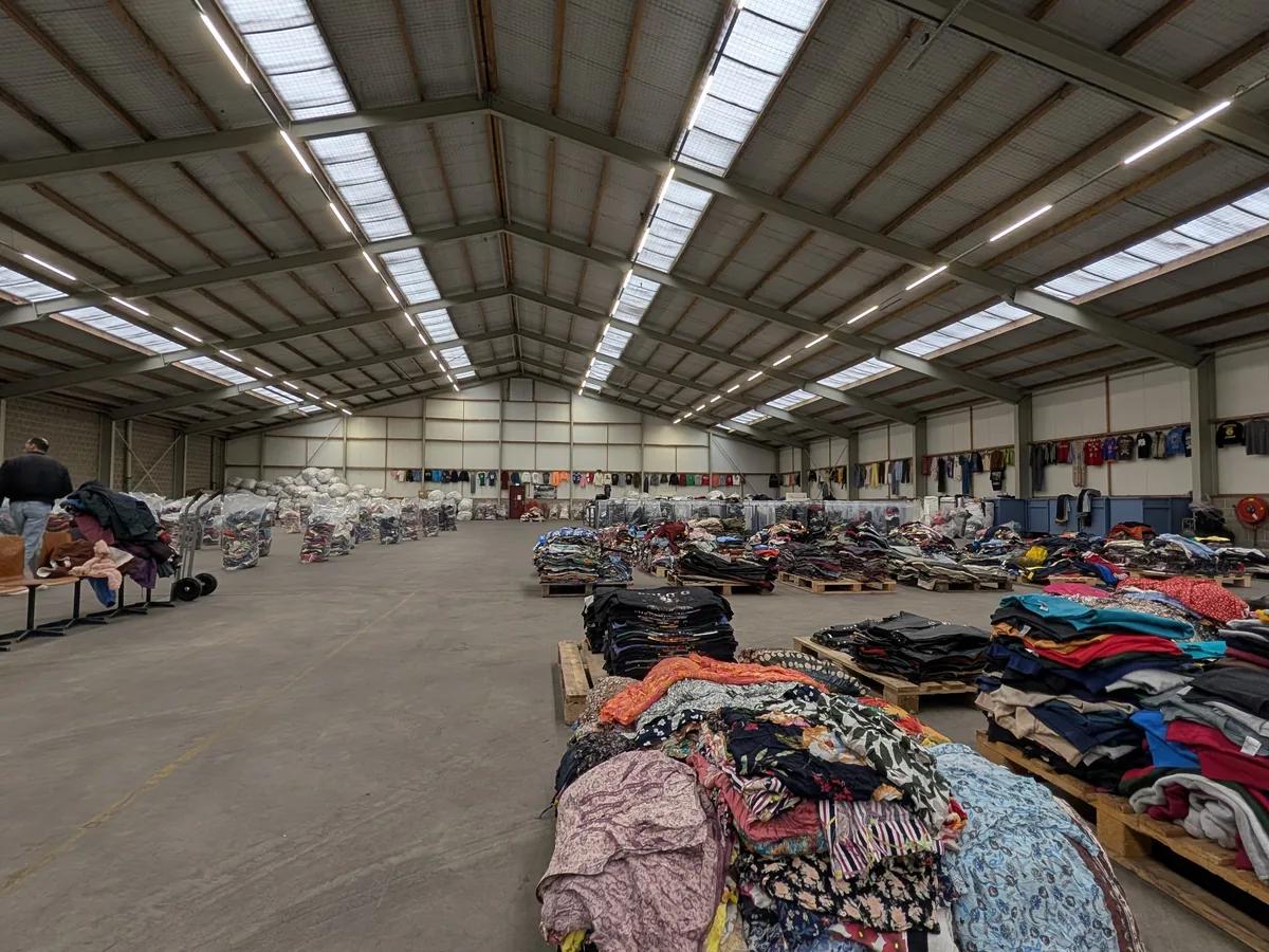Gang met balen en gesorteerde tweedehands kleding op de warehousevloer in Bovenkarspel