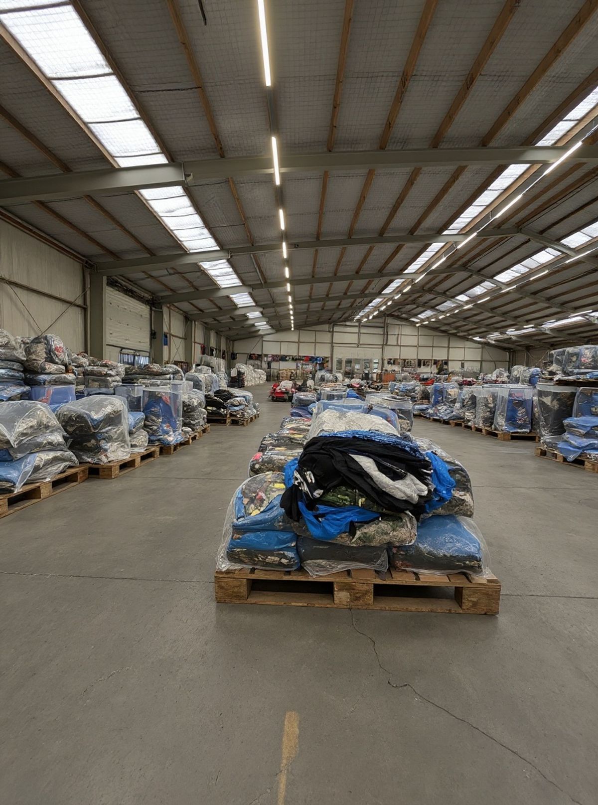Reseller loopt langs gesorteerde tweedehands kleding balen op de warehousevloer van Excellent Vintage in Bovenkarspel