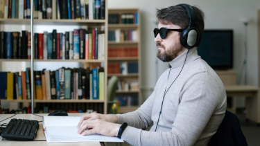 A Blind Man Wearing Headset while Using Braille