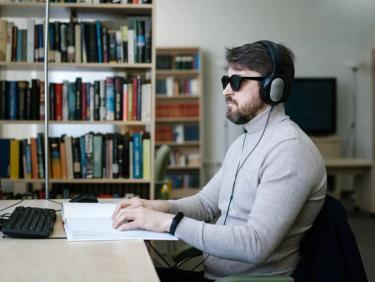 A Blind Man Wearing Headset while Using Braille