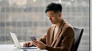 Man using laptop whilst looking at mobile phone