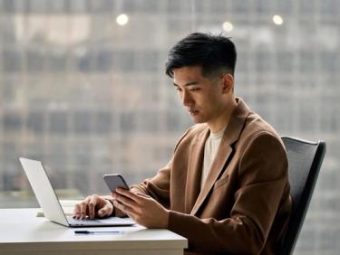 Man using laptop whilst looking at mobile phone